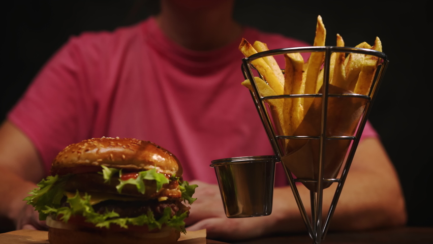 Man eats french fries dipping into sauce in burger joint.