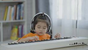 Asian cute girl wearing white headphone learning and playing piano music in the living room at home. The idea of activities for the child at home during quarantine. Music learning study online concept
