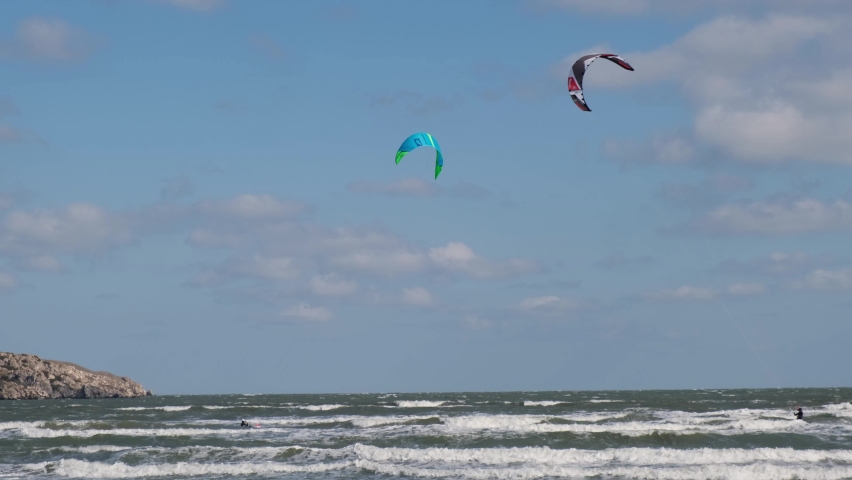 A man in a wetsuit on a parachute rides a board on the waves of the sea. A young man performs a trick in the air against the sky. Water sports, kitesurfing, paragliding, hydrofoil, surfing. Kiteboarde Royalty-Free Stock Footage #1097102521