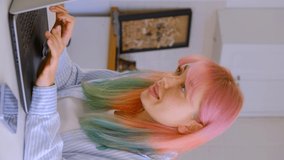 Happy young female communicating online. Vertical stock video of cheerful white woman with colored hair typing text and laughing