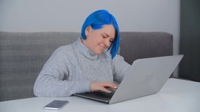 Happy blue haired woman typing text on laptop keyboard. Cheerful Ukrainian female working on modern notebook computer at home