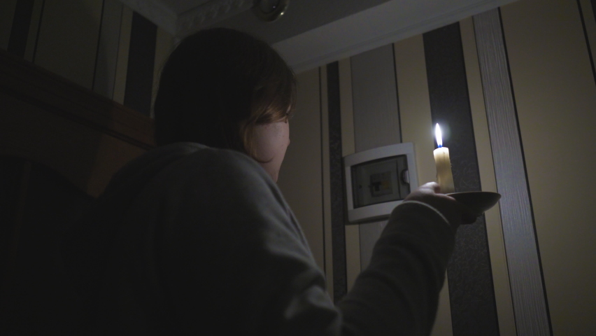 Blackout Energy crisis. Power outage concept. A girl with a burning candle in a dark room sits by the window and looks into the darkness on the street. Fixed Camera Royalty-Free Stock Footage #1097107035