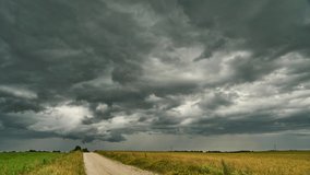 A timelapse storm over a field and a dirt road. Gray rain clouds are raging over a wheat field. The hurricane threatens to destroy crops. Time lapse cloud movement - Powered by Shutterstock - Get 15% off with code: PIKWIZARD15
