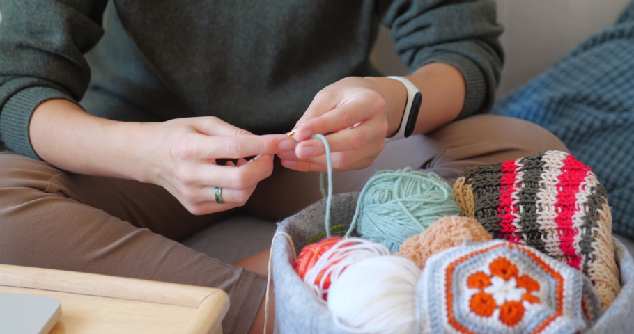 Close-up video of woman learning to crochet. Felt basket with balls of yarn. Anti-stress hobby. Online lessons for amateurs on laptop.