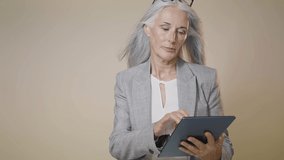 Cinematic video of a beautiful senior business woman in studio. Middle aged woman with silver hair and elegant suit posing for a corporate session
