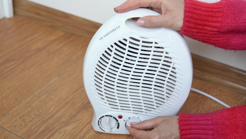 Woman hands in a red sweater adjusting electric fan heater in room and checks with his hand if there is heat. Girl turns on the portable fan heater to heat the room. Autonomous electric space heating Royalty-Free Stock Footage #1097112117