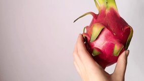 Dragon fruit in a woman hand. Turning around slice white pulp with seeds. Pitaya exotic healthy fruit diet. Asian Thai pitahaya half section on gray background isolated close up free space video