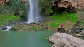 Woman is holding a mobile phone and taking a photo of a beautiful waterfall. Slow motion full HD video. 
