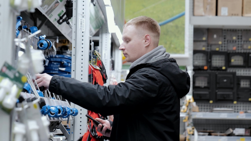Young man in a hardware store. A man in a store chooses accessories for watering the lawn. Construction supermarket. Big hardware store Royalty-Free Stock Footage #1097123689