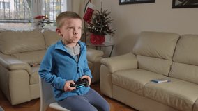 A five-year-old boy plays a game console near a Christmas tree