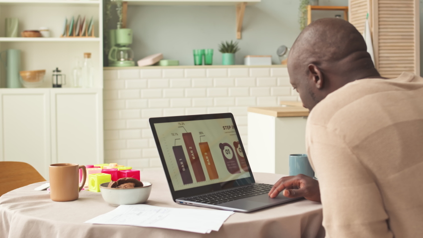 Black man looking at presentation slide on marketing infographics while working on laptop from home sitting at kitchen table