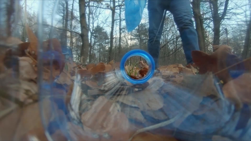 A man picking up a plastic bottle and putting it in a blue garbage bag in the park, pov view from inside of the bottle. The concept of plastic pollution, forest cleaning. 
 | Shutterstock HD Video #1097125587