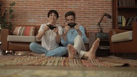 Middle aged hispanic couple sitting on the living room carpet playing video games with the console controller.