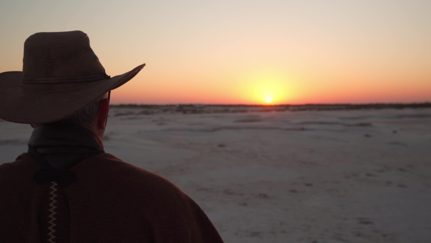 close up of a man dressed as a cowboy standing on a salt field watching the sunrise Royalty-Free Stock Footage #1097131043