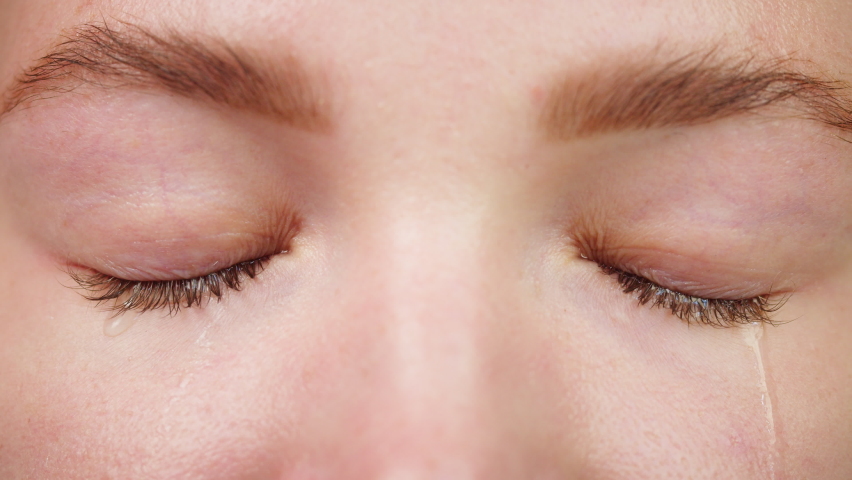 Close-up of crying blue eyes, watery eye of young woman, shooting of tears rolling down the cheeks. Feeling pain and sadness, weeping.