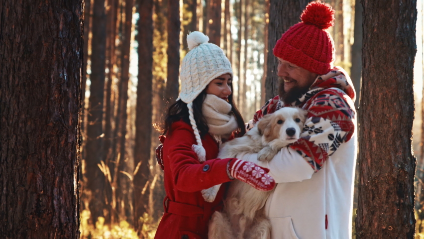 Family Christmas weekend spend time together. Happy young couple of man and woman in warm coat and hat walking in winter forest with their doggy. Love hug. Christmas eve and New Year holidays concept. Royalty-Free Stock Footage #1097141059