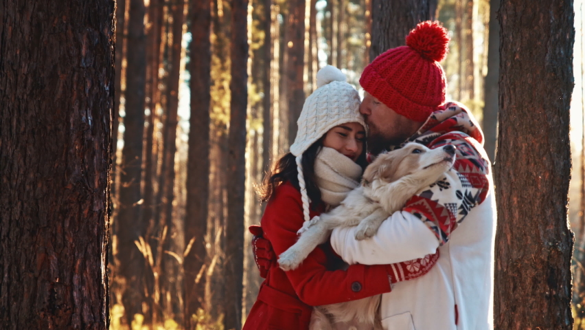 Family Christmas weekend spend time together. Happy young couple of man and woman in warm coat and hat walking in winter forest with their doggy. Love hug. Christmas eve and New Year holidays concept. | Shutterstock HD Video #1097141059