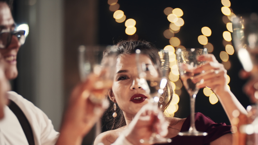 Happy festive group of friends drinking alcohol celebrating Christmas New Year waving sparklers. Close up hands cheers champagne clinking glasses. Smiling multiethnic people at Christmas eve night. Royalty-Free Stock Footage #1097141071