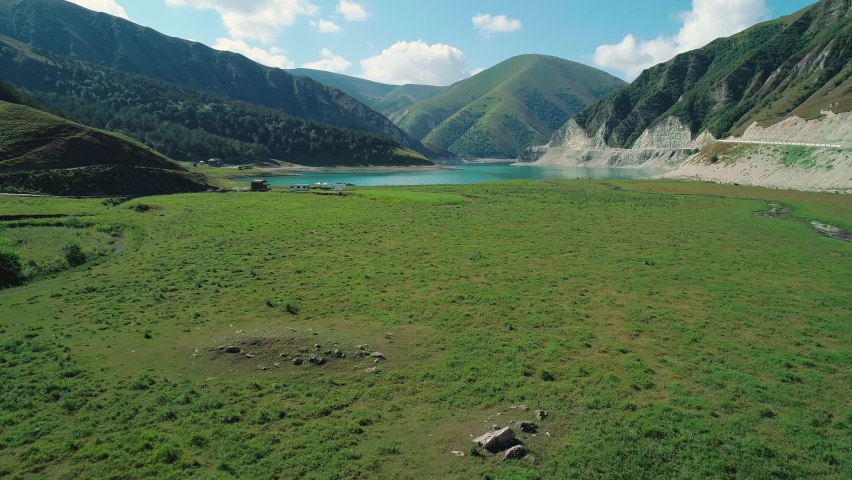 Aerial over green valley in front of lake Kezenoy-am with turquoise water and tall mountains around. Stunning scenery in highlands of Chechen Republic, Russia