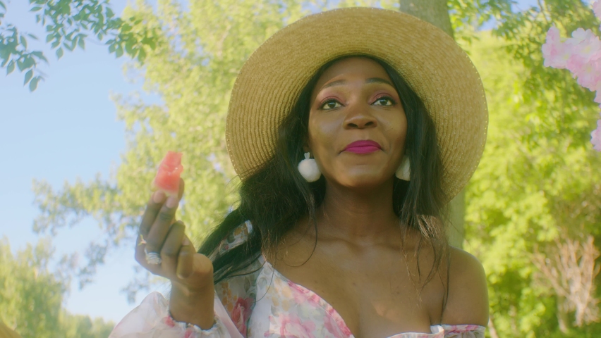 Happy smiling black lady eats watermelon in park - picnic in shade of trees
