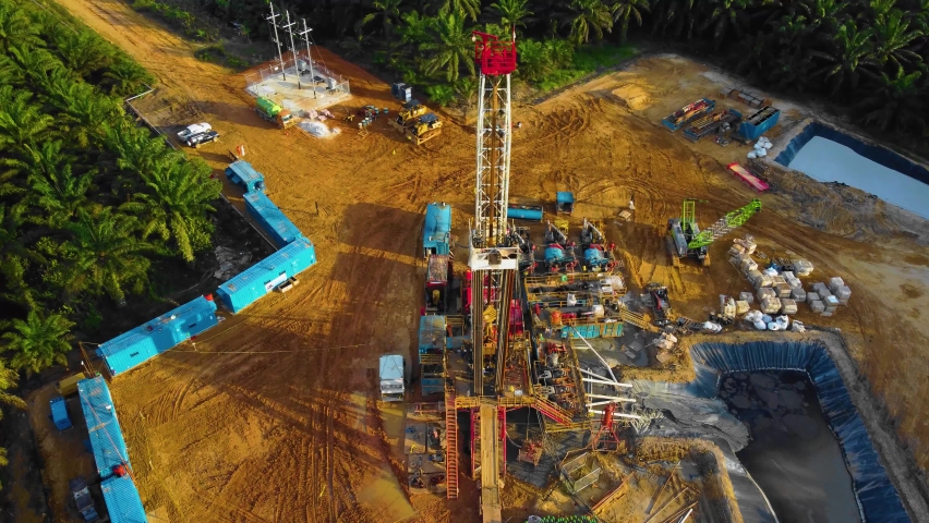 Cinematic 4K Drone Footage of Onshore Drilling Rig equipment structure for oil exploration and exploitation in the middle of jungle surrounded by palm oil trees during sunset and high oil price. Royalty-Free Stock Footage #1097145817