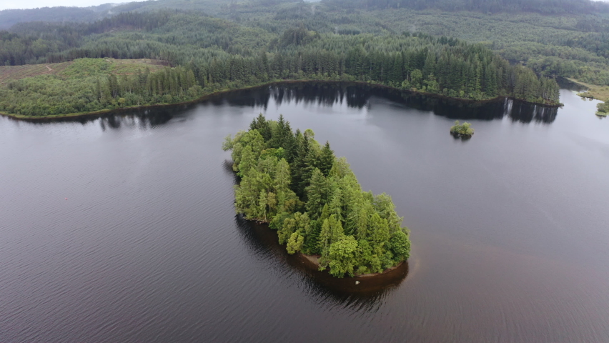 Aerial view of a small island covered in trees in the middle of a Scottish loch on a cloudy day.