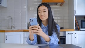 Cheerful Vietnamese girl browsing mobile app on smartphone. Happy Asian female using modern blue cellphone for communication. BIPOC person lifestyle video clip 