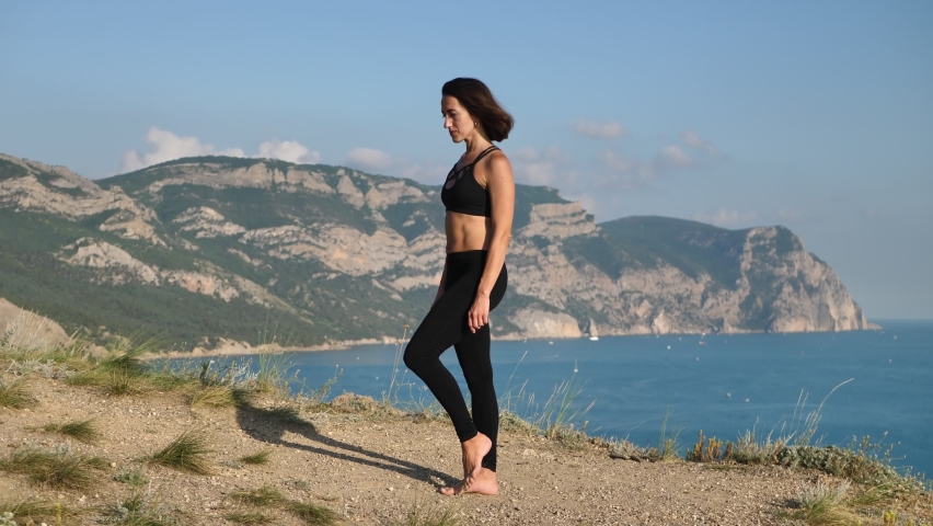 Meditation in a complex yoga pose, balancing on the edge of a cliff overlooking the sea at dawn | Shutterstock HD Video #1097156379