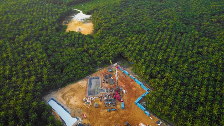 Cinematic 4K Drone Footage of Onshore Drilling Rig equipment structure for oil exploration and exploitation in the middle of jungle surrounded by palm oil trees during sunset and high oil price.