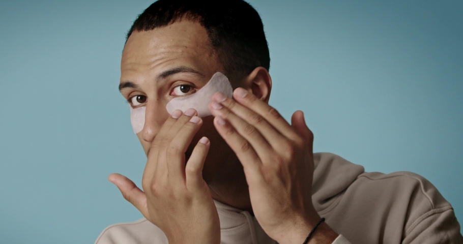 Skin care. Portrait of male model applying under eye patches. Beauty cosmetic mask on face. Face care routine. Cosmetology facial treatment  | Shutterstock HD Video #1097159395