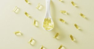 Video of oil capsules with white spoon on yellow background with copy space. Medicine, medical services, healthcare and health awareness concept.