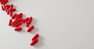Video of white pill box spilling red pills on white background with copy space. Medicine, medical services, healthcare and health awareness concept.