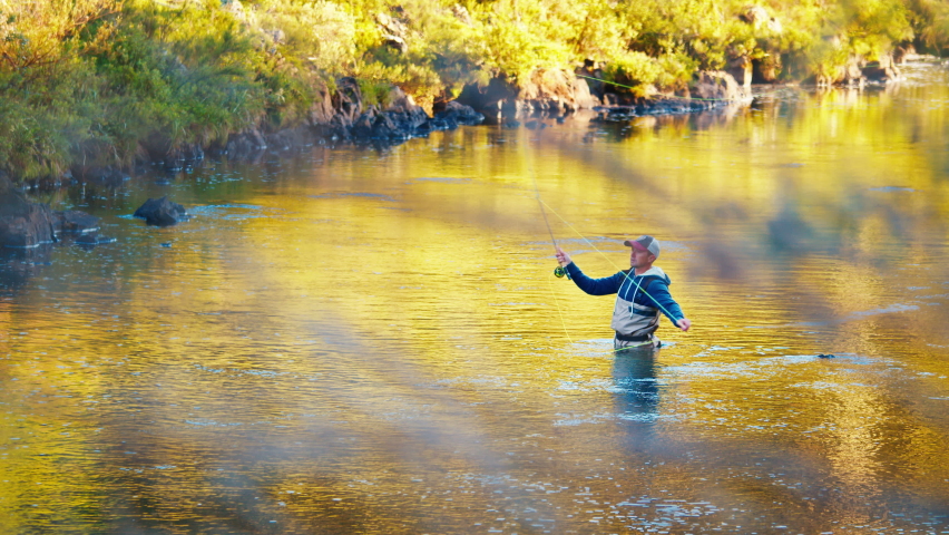 Fisherman casts the line on a river at sunrise. Angler stands in waders in the river and fishing on fly
