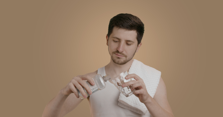 Young man with perfect clean skin wears white tank top, rinses mouth with toothpaste, isolated on plain pastel beige background studio portrait. Male personal hygiene concept | Shutterstock HD Video #1097166915