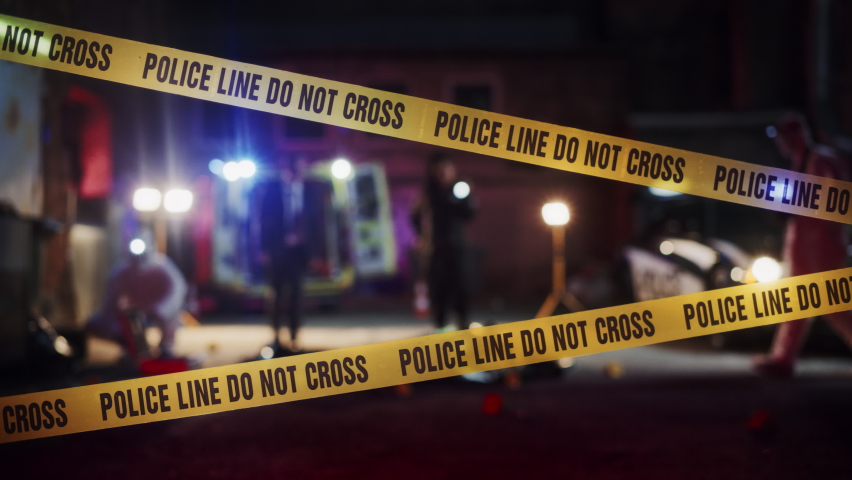 Zoom Into a Crime Scene at Night: Crime Scene Investigation Team Working on a Murder. Female Police Officer Briefing Detective on the Victim's Body. Forensics and Paramedics Working. Cinematic Shot Royalty-Free Stock Footage #1097167457