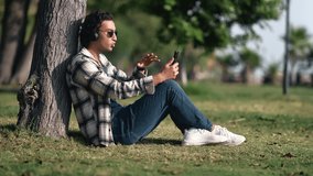 Relaxed Hispanic modern guy talking online video call to friends relatives use smartphone headphones at summer park. Cheerful Arabic man discussing on mobile phone resting at nature garden 