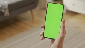 Handheld Camera: Point of View of Young Woman at Home Sitting on Living Room With Green Mock-up Screen Smartphone. Girl is Watcing Content Without Touching Gadget Screen. Modent Technology