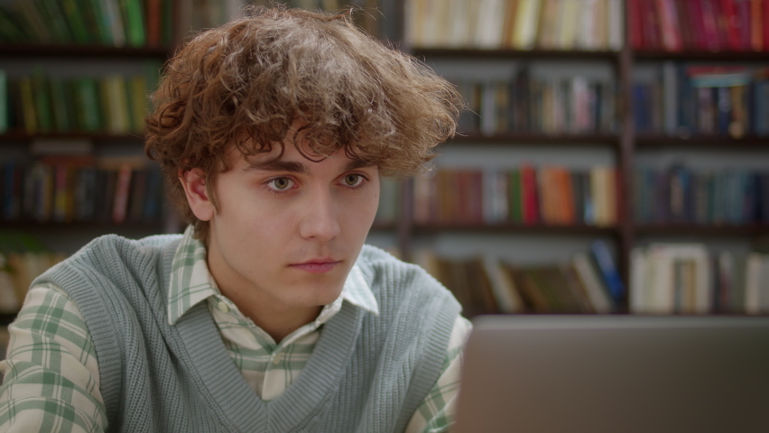 Attractive Student Man Using Laptop Search Information Internet Course Study Online e Learning in App Looking at Laptop Monitor Doing Research For Test Exam Sit at Library Desk.