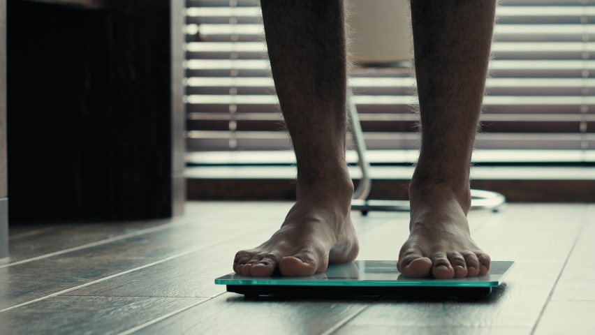 Close-up male legs foots standing on electronic scales weight control. Sporty unrecognizable guy man athlete barefoot checking body kilograms check results of sport training workout and healthy eating | Shutterstock HD Video #1097174995