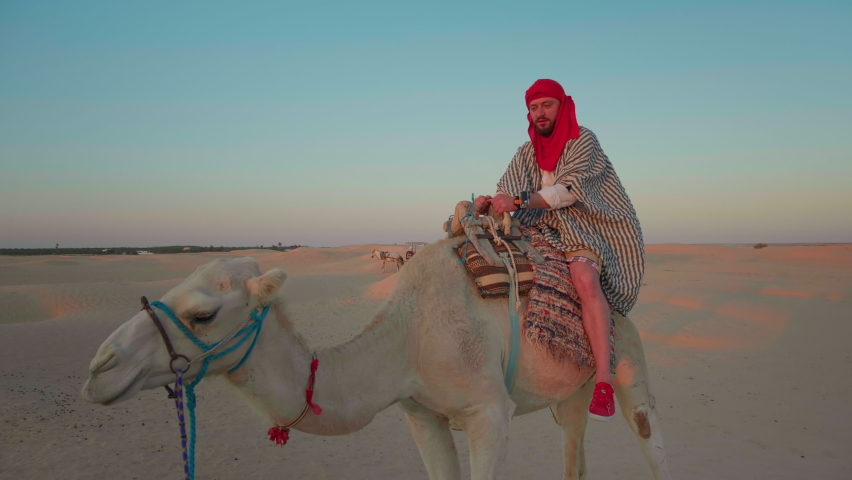 Tourist on camel in desert enjoying his ride wearing red turban. Male sharing his point of view about his first camel ride.