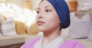 Video of tranquil biracial woman in hijab doing yoga meditation, closing eyes and deep breathing. Happiness, health, fitness, inclusivity and domestic life.