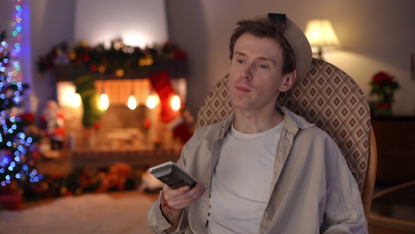 Bored lonely LGBT man switching channels with remote control sitting in rocking chair in living room on Christmas eve. Portrait of young guy watching TV at home on New Year alone | Shutterstock HD Video #1097176141