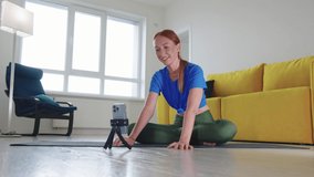 Athletic woman sits on yoga mat and shoots a video on the front camera of the phone