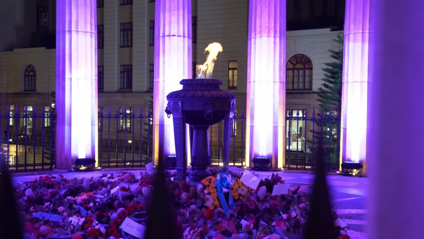 Illuminated Shrine of Remembrance with burning eternal flame, flowers on the ground honouring the dead, candlelight vigil night before Anzac day, Brisbane city, Queensland, handheld motion shot.