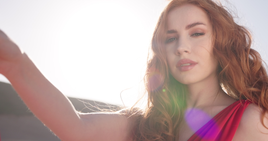 Face of Beautiful Ginger Caucasian Woman Looking at Camera Cute Smiling. Portrait Young Caucasian Pretty Redhead Girl Outside at Sunshine. Wind Blowing Her Red Dress. Young Woman Face. Beauty Concept Royalty-Free Stock Footage #1097180415