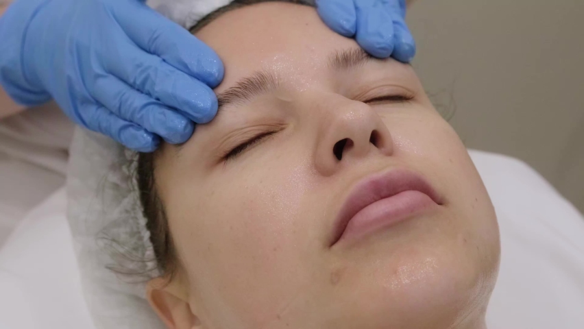 Manual facial massage. Young beautiful woman getting professional skin care at spa salon. Close-up, beautician in gloves makes anti-aging face massage to female patient. | Shutterstock HD Video #1097181013