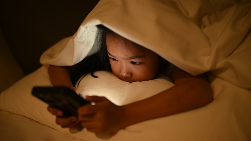 Asian kid playing game on smartphone in the bed at night,The girl Addict social media