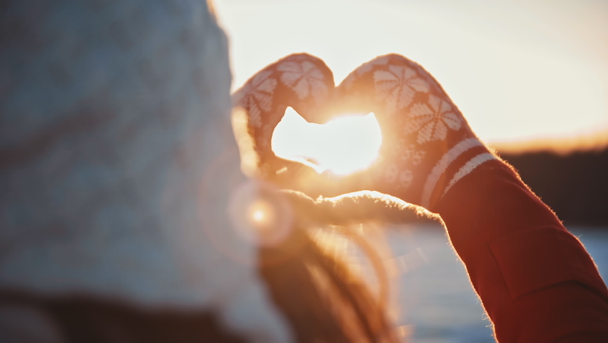 Heart valentine day Woman wearing gloves make Love heart shape from hands at morning winter sunrise. Happy Christmas time. Light of sunset sun in hands at frosty cold snowy day. Christmas New Year