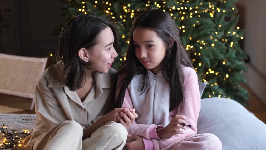 Two cute sisters, friends share the news, whisper secrets in your ear, sitting on the bed against the backdrop of the Christmas tree. Cute children celebrate winter holidays. Festive mood. | Shutterstock HD Video #1097185349