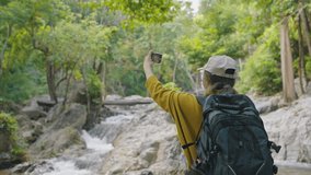 Asian young woman hiking and backpack wearing yellow sweater using smartphone video call in the forest